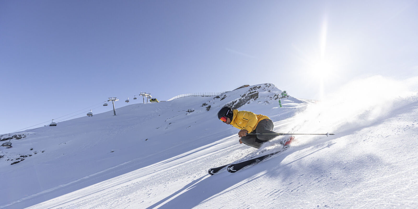 Mann fährt bei schönem Wetter mit den Skiern eine steile Piste hinunter